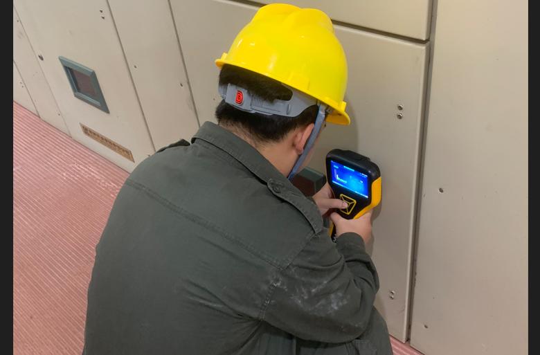 Field engineer using a handheld partial discharge detector to scan high-voltage switchgear panels for insulation defects.